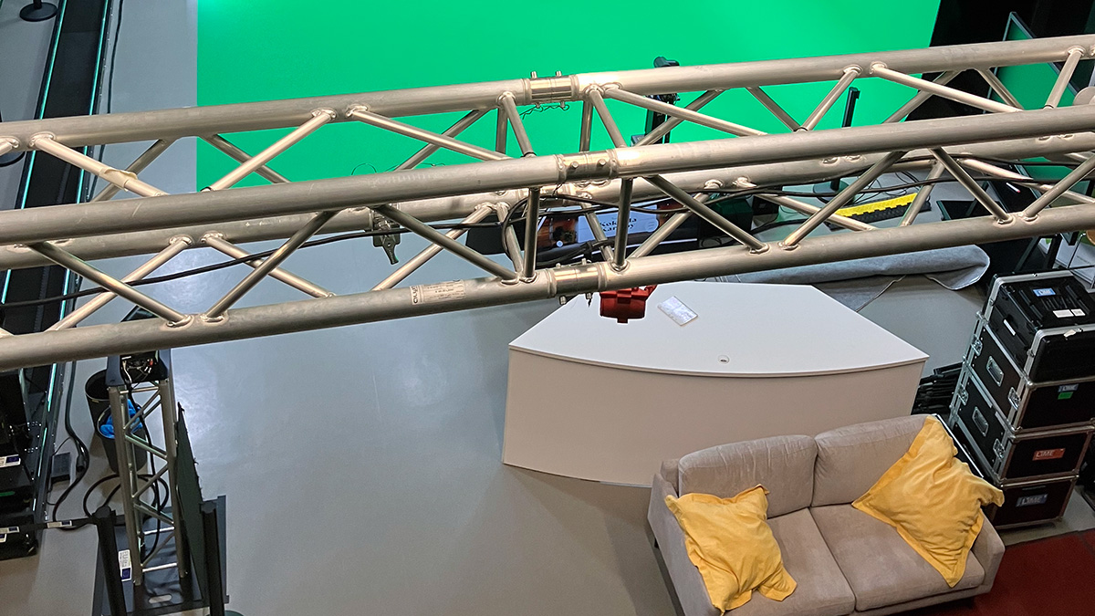 Green screen ‑studio ylhäältä päin nähtynä, etualalla katosta riippuva trussi, lattia­ta­sossa vihreää pintaa, sohva ja valai­su­ka­lustoa
