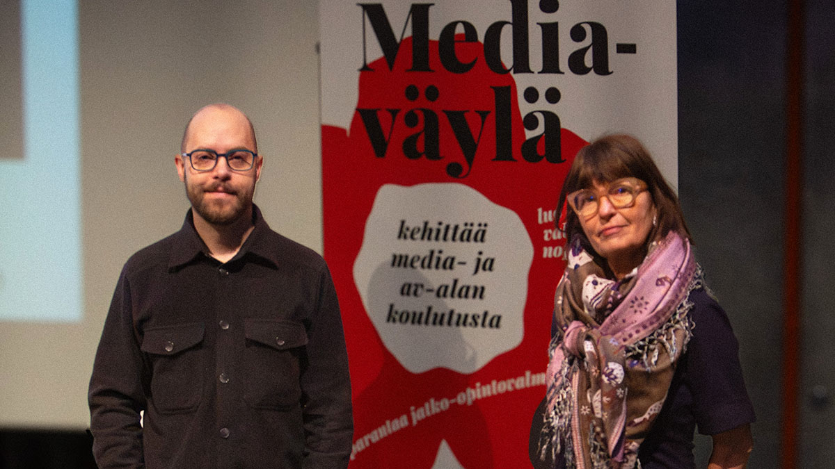 Kaksi henkilöä seisoo Mediaväylän roll-upin edessä